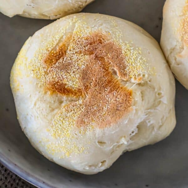 A close-up of a baked roll with a lightly browned top and sprinkled cornmeal on a plate.