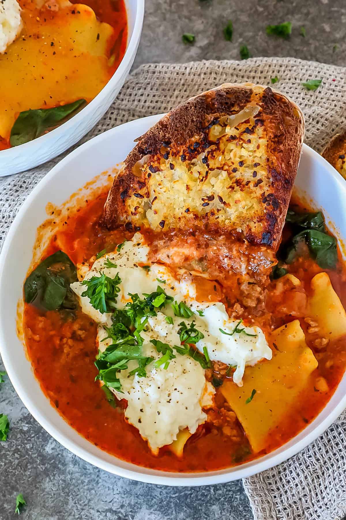 Bowl of lasagna soup with spinach, cheese, and herbs, topped with a slice of toasted bread.