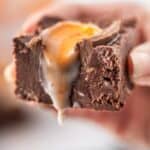 A close-up captures a hand cradling a piece of chocolate fudge, reminiscent of the gooey delight found in a Cadbury Egg, with caramel sauce tantalizingly oozing from its center.