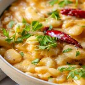 A close-up of creamy pasta infused with garlic, topped with red chili peppers and garnished with fresh parsley.