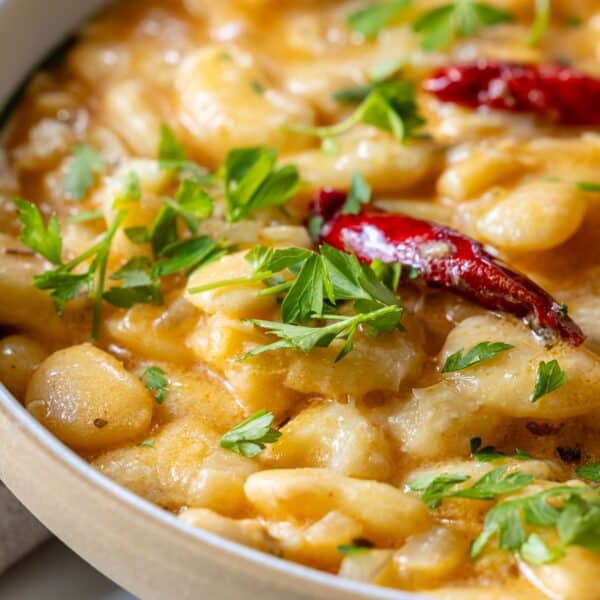 A close-up of creamy pasta infused with garlic, topped with red chili peppers and garnished with fresh parsley.