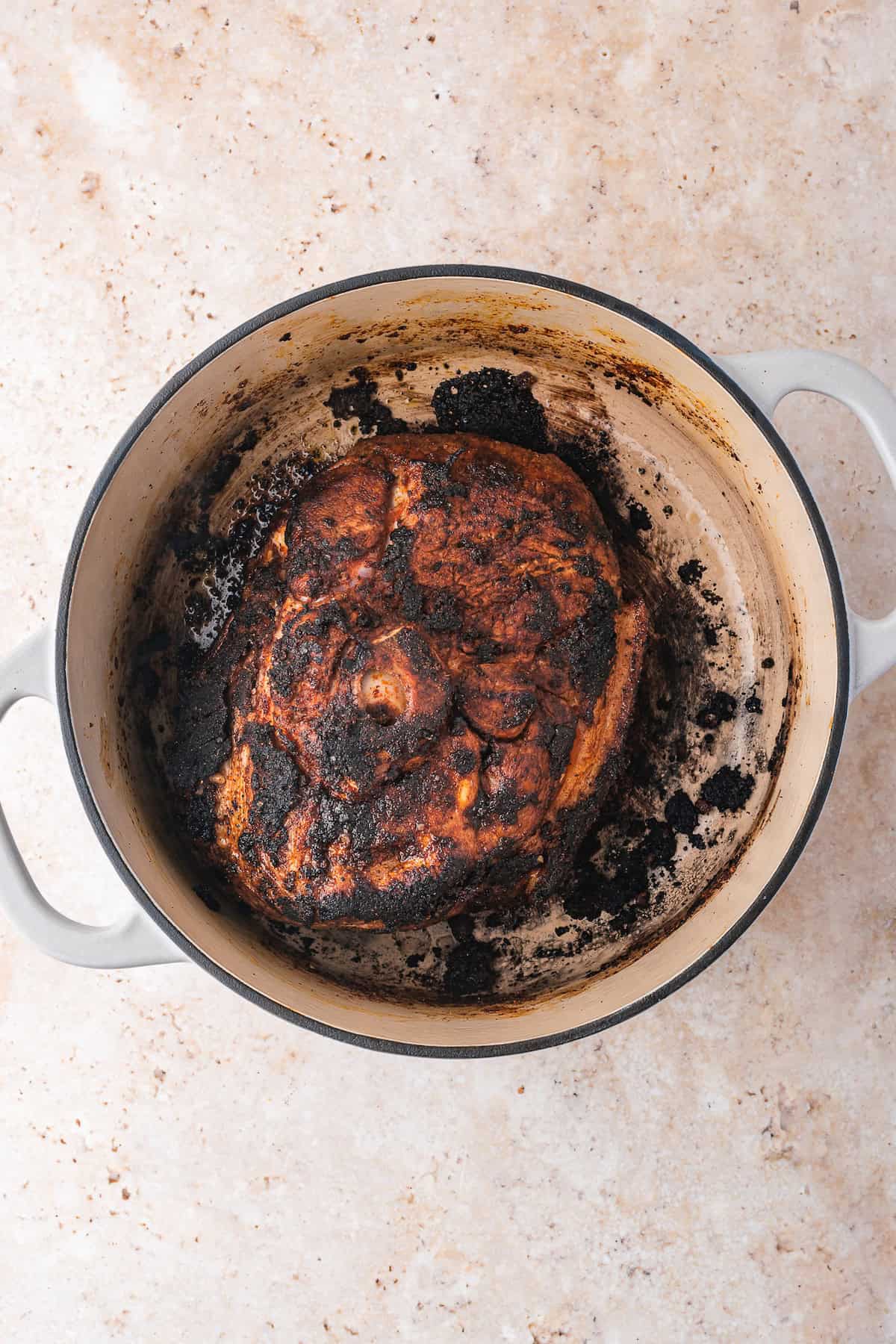 A burnt roast sits in a Dutch oven on a light marble surface, embodying rustic charm.