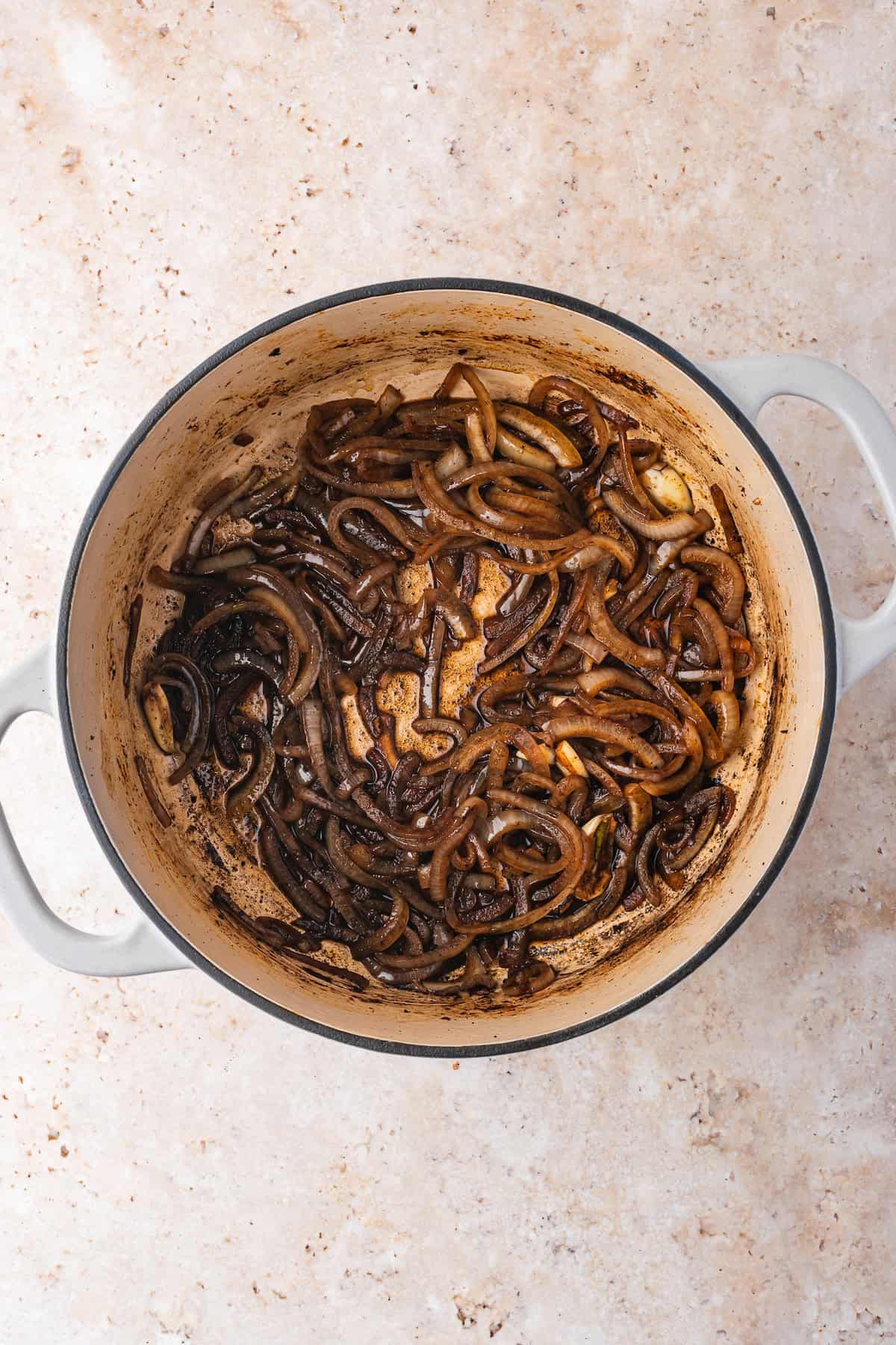 Sautéed onions in a Dutch Oven, browned and caramelized, on a speckled countertop.