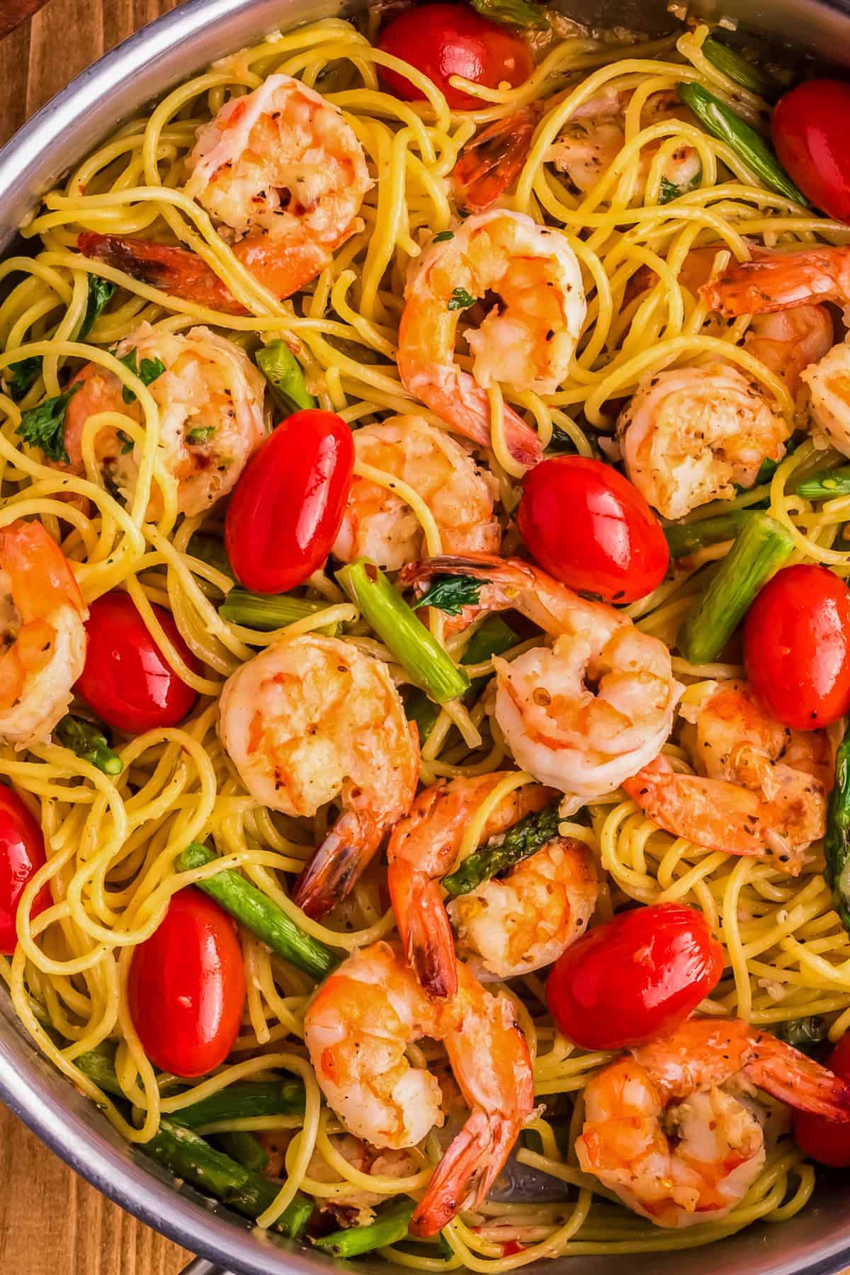 A close-up of a pan filled with perfectly cooked pasta featuring succulent shrimp, vibrant cherry tomatoes, and tender asparagus subtly infused with the rich aroma of garlic.