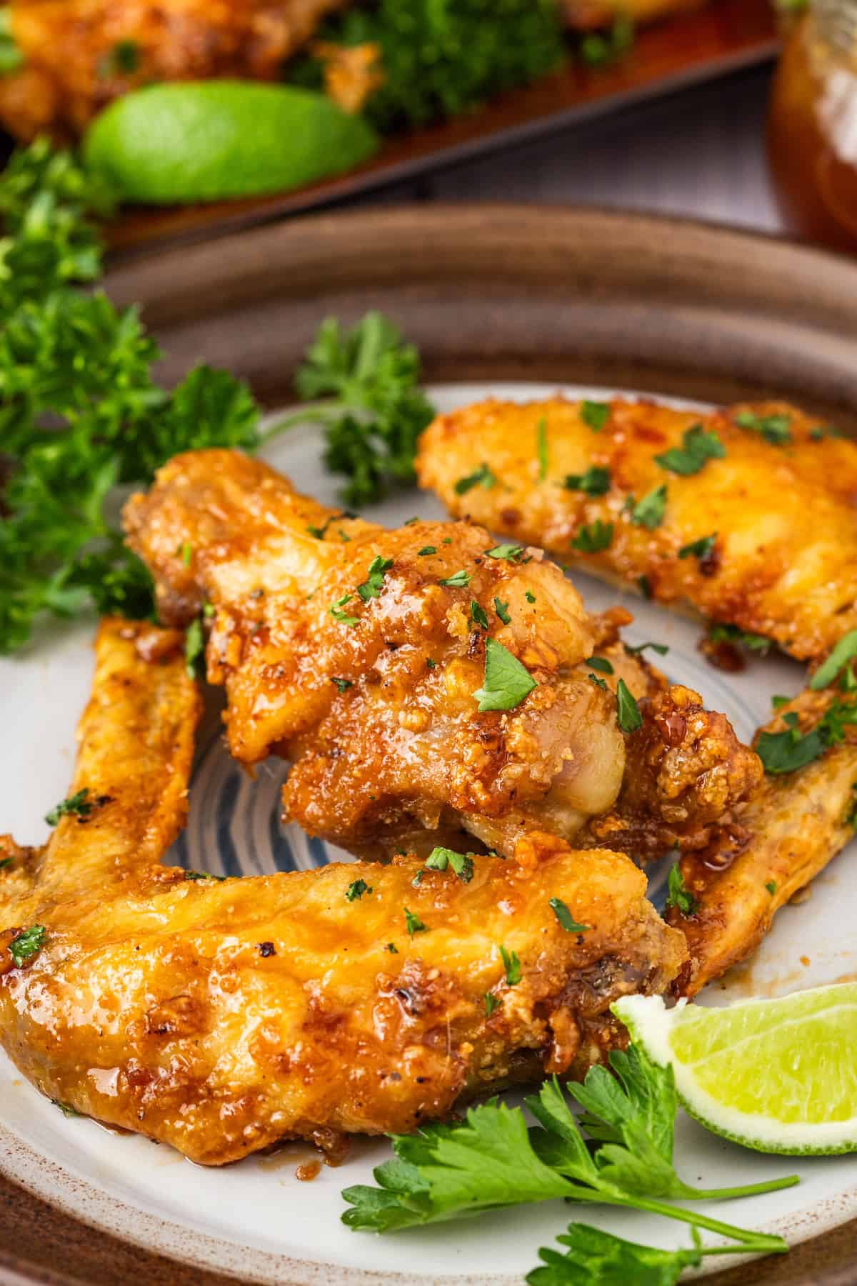 Close-up of three succulent chicken wings glazed with honey and garlic, garnished with parsley on a plate, accompanied by lime wedges and additional parsley.