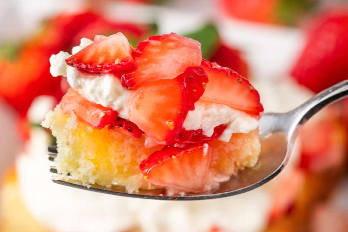 A delightful spoonful of cake featuring strawberry shortcake with sliced strawberries and whipped cream.