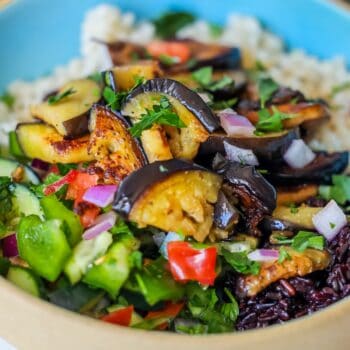 A savory sabich bowl featuring a bed of rice piled high with roasted eggplant, fresh diced vegetables, and vibrant herbs—a perfect vegan delight.