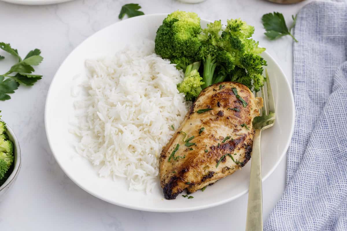 A plate with Ranch Chicken Breasts, steamed broccoli, and white rice, served with a gold fork on a white surface.