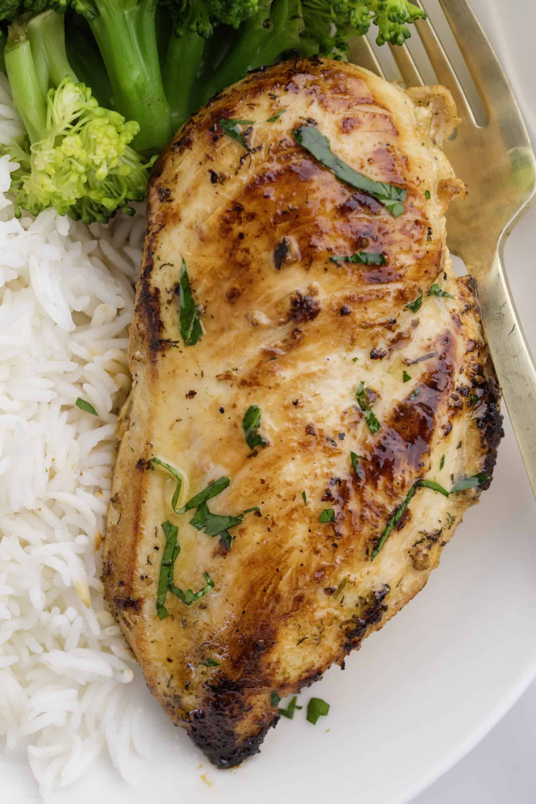 A delicious Ranch Chicken Breast garnished with herbs, served alongside white rice and steamed broccoli on a white plate with a fork.