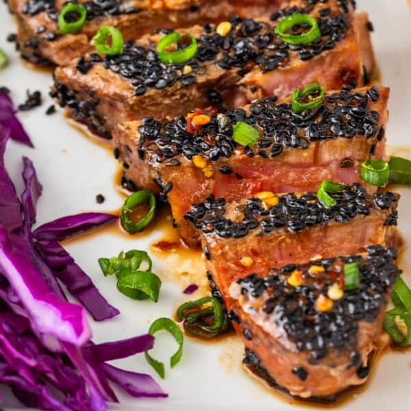 Seared Ahi Tuna sliced and coated with black sesame seeds, garnished with chopped green onions, and served atop shredded purple cabbage on a white plate.
