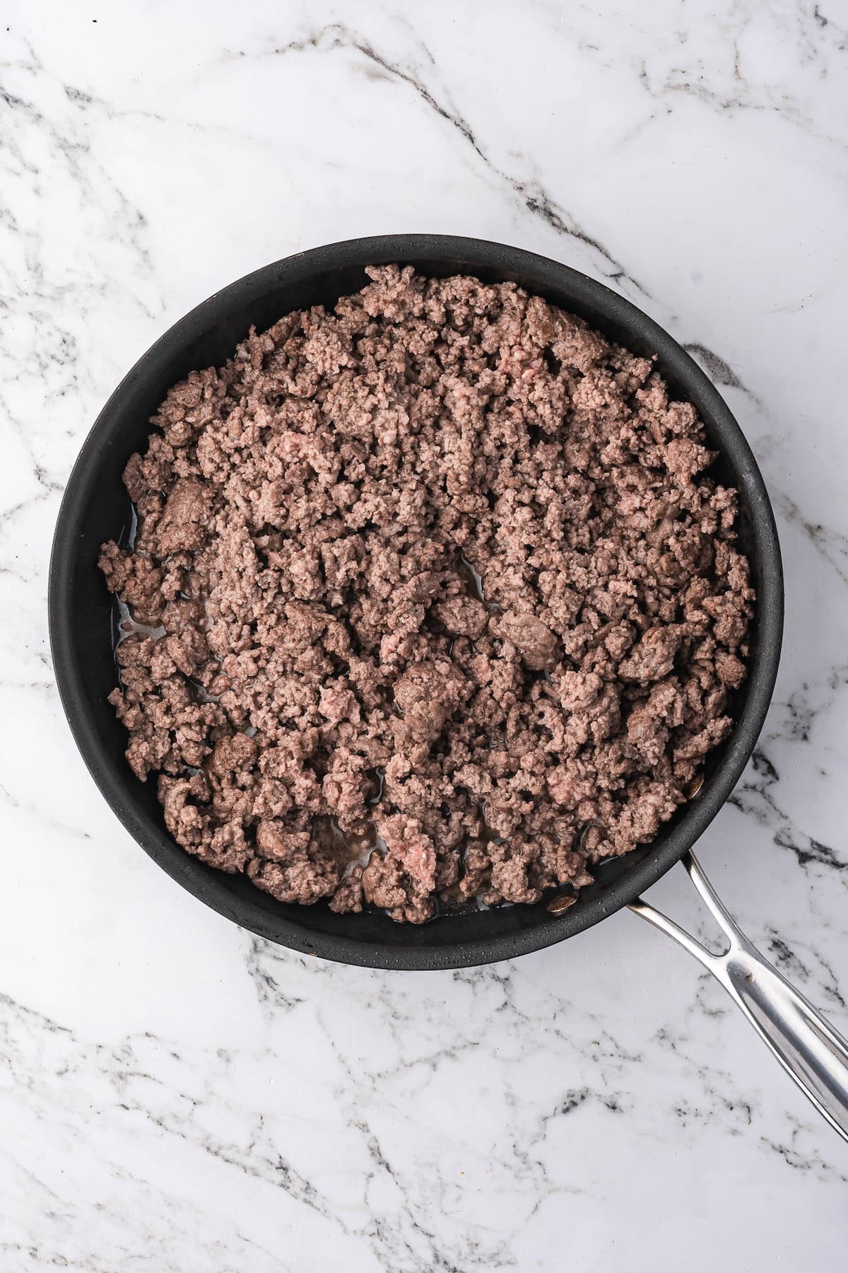 A frying pan filled with cooked ground beef for beef stroganoff sits on a white marble countertop.