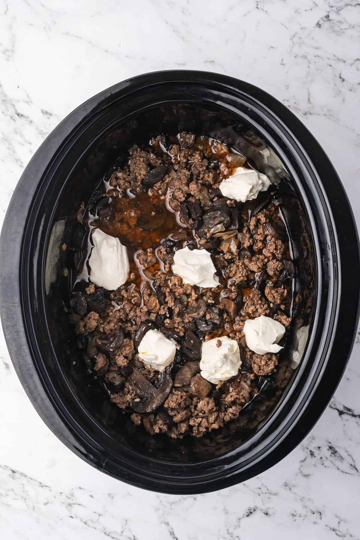 Slow Cooker Beef Stroganoff with ground beef and mushrooms, topped with dollops of sour cream, served fresh on a marble countertop.