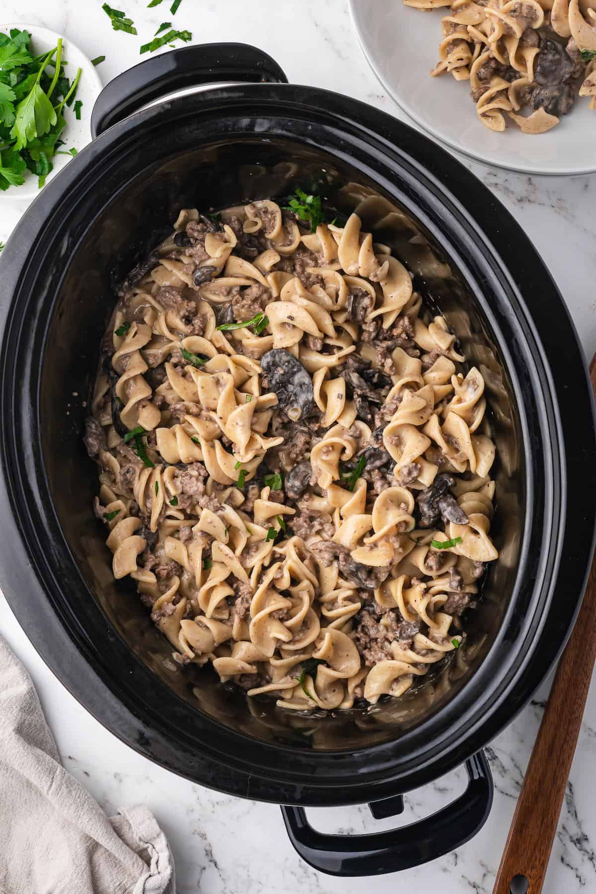 A slow cooker filled with Slow Cooker Beef Stroganoff made with tender beef, egg noodles, and mushrooms, garnished with chopped parsley.