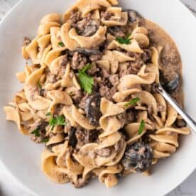 A plate of Slow Cooker Beef Stroganoff with egg noodles, ground beef, mushrooms, creamy sauce, and parsley garnish is served with a fork.