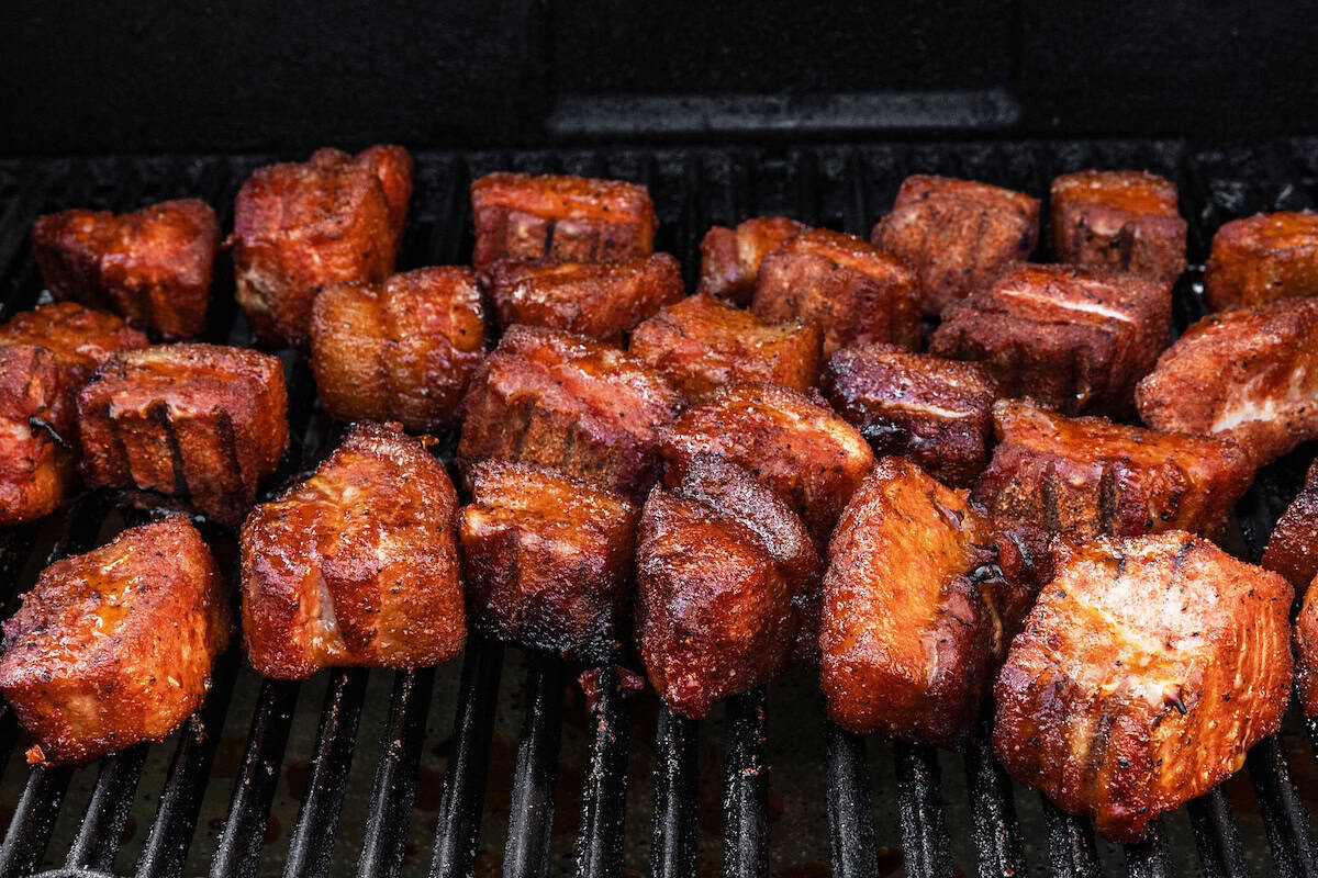 Close-up of several cubes of BBQ Pork Belly burnt ends cooking on a grill.