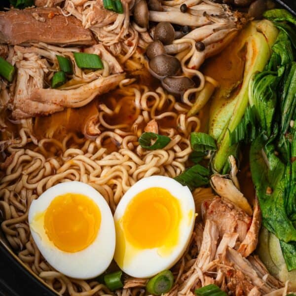 Bowl of Chicken Ramen with noodles, soft-boiled egg halves, shredded slow cooker chicken, mushrooms, bok choy, green onions, and rich broth.