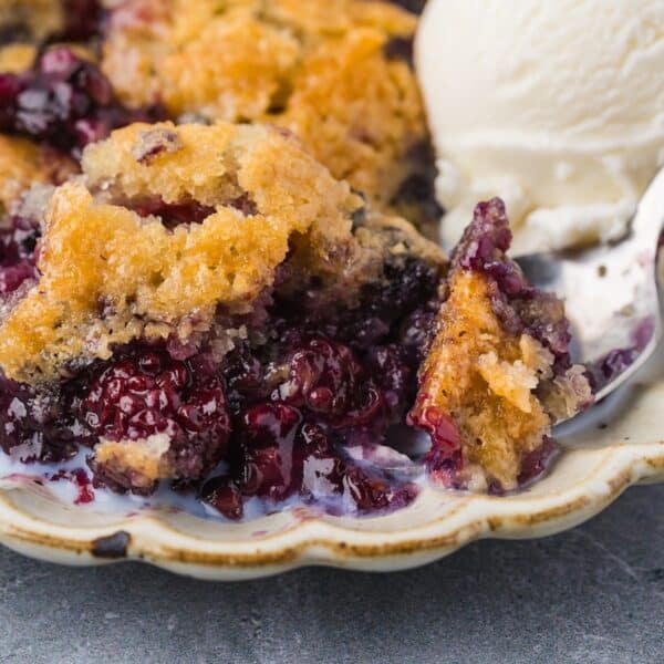 A close-up of a serving of Smoked Berry Cobbler topped with vanilla ice cream on a decorative plate.