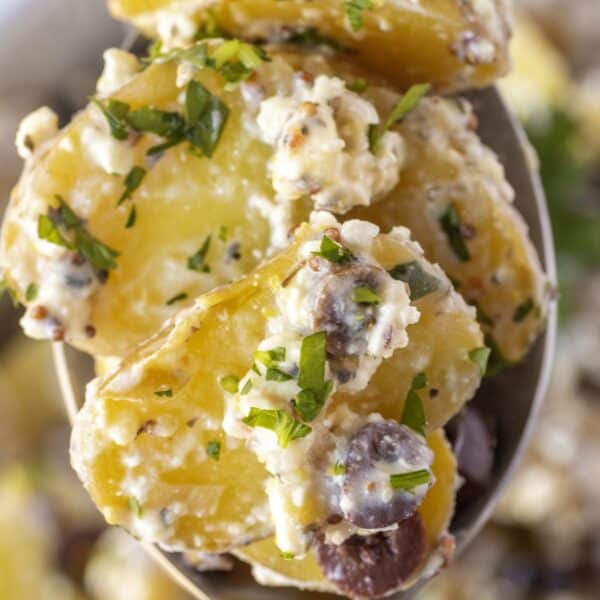 Close-up of Greek Potato Salad featuring sliced potatoes mixed with feta cheese, black olives, and chopped parsley.