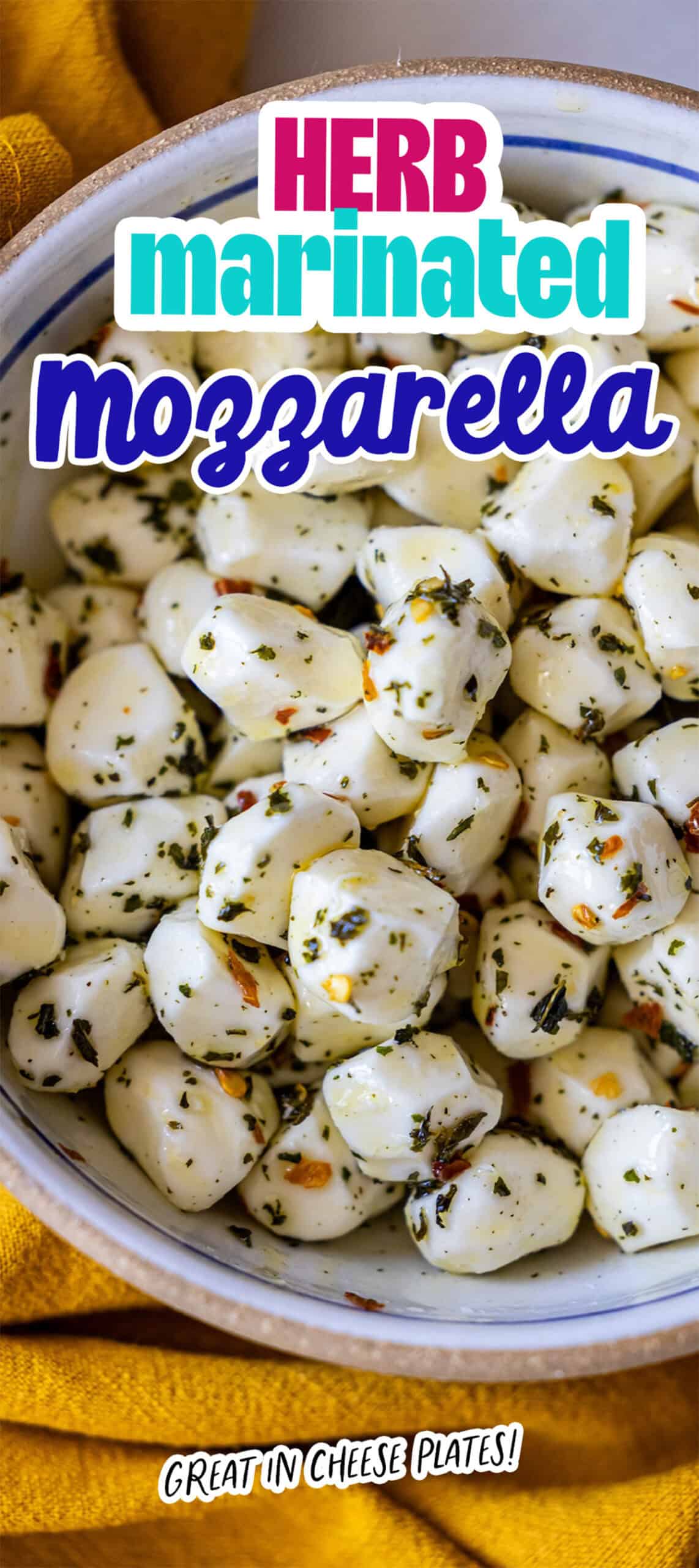 A bowl of herb marinate mozzarella balls, seasoned with herbs and spices, placed on a yellow cloth. Text reads: “Herb marinated mozzarella balls. Great in cheese plates!”.