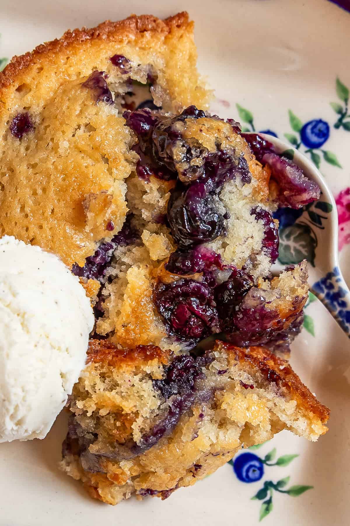Sour-Sweet Sourdough Blueberry Cobbler 5 A serving of sourdough blueberry cobbler with a scoop of vanilla ice cream on a floral plate.