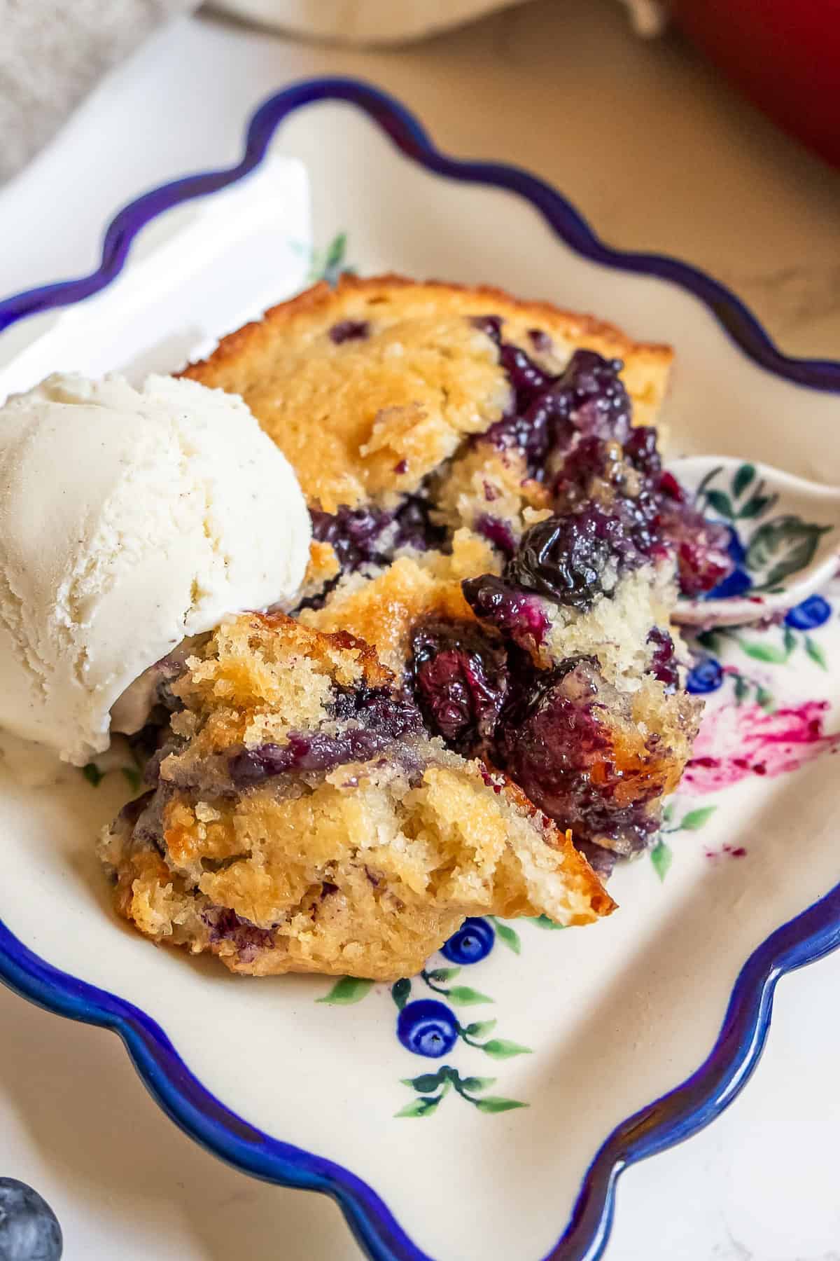 Sour-Sweet Sourdough Blueberry Cobbler 4 A slice of sourdough blueberry cobbler served on a floral plate with a scoop of vanilla ice cream.