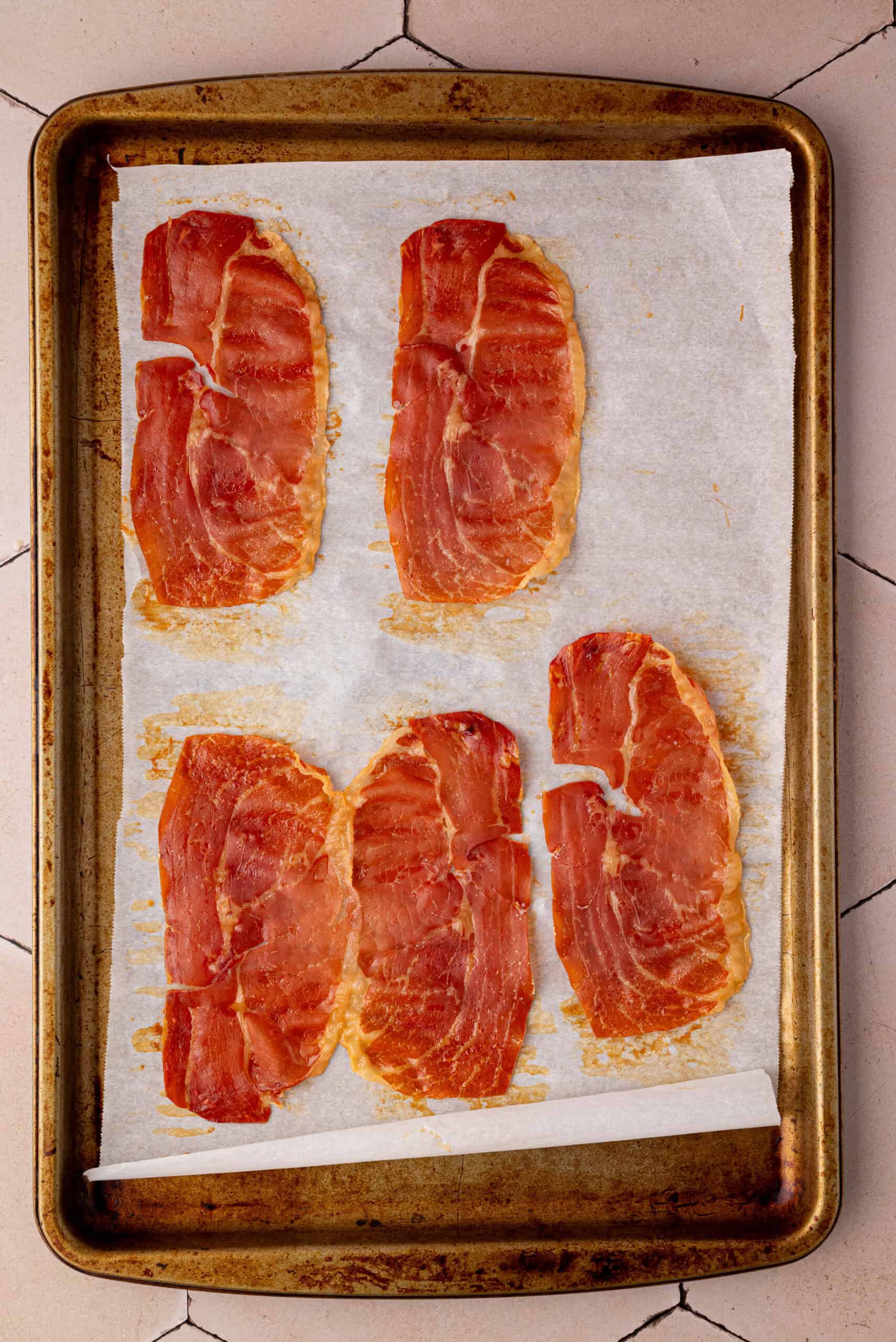 Five slices of cooked bacon are arranged on a parchment-lined baking sheet, set on a tiled surface—perfect for serving alongside a refreshing Summer Fruit Caprese Salad.