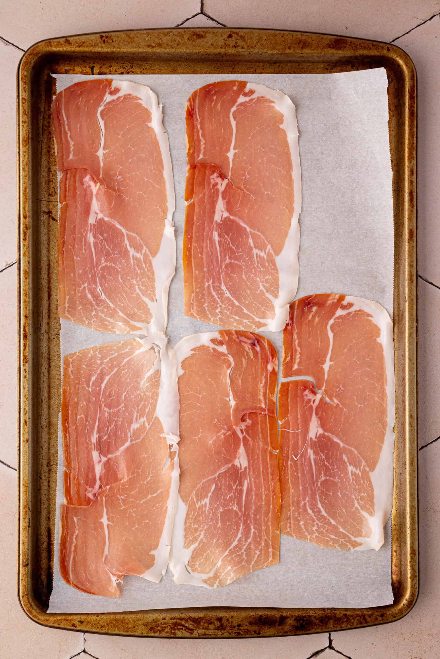 Six slices of prosciutto are arranged on a parchment-lined baking sheet, ready to complement a fresh Summer Fruit Caprese Salad.