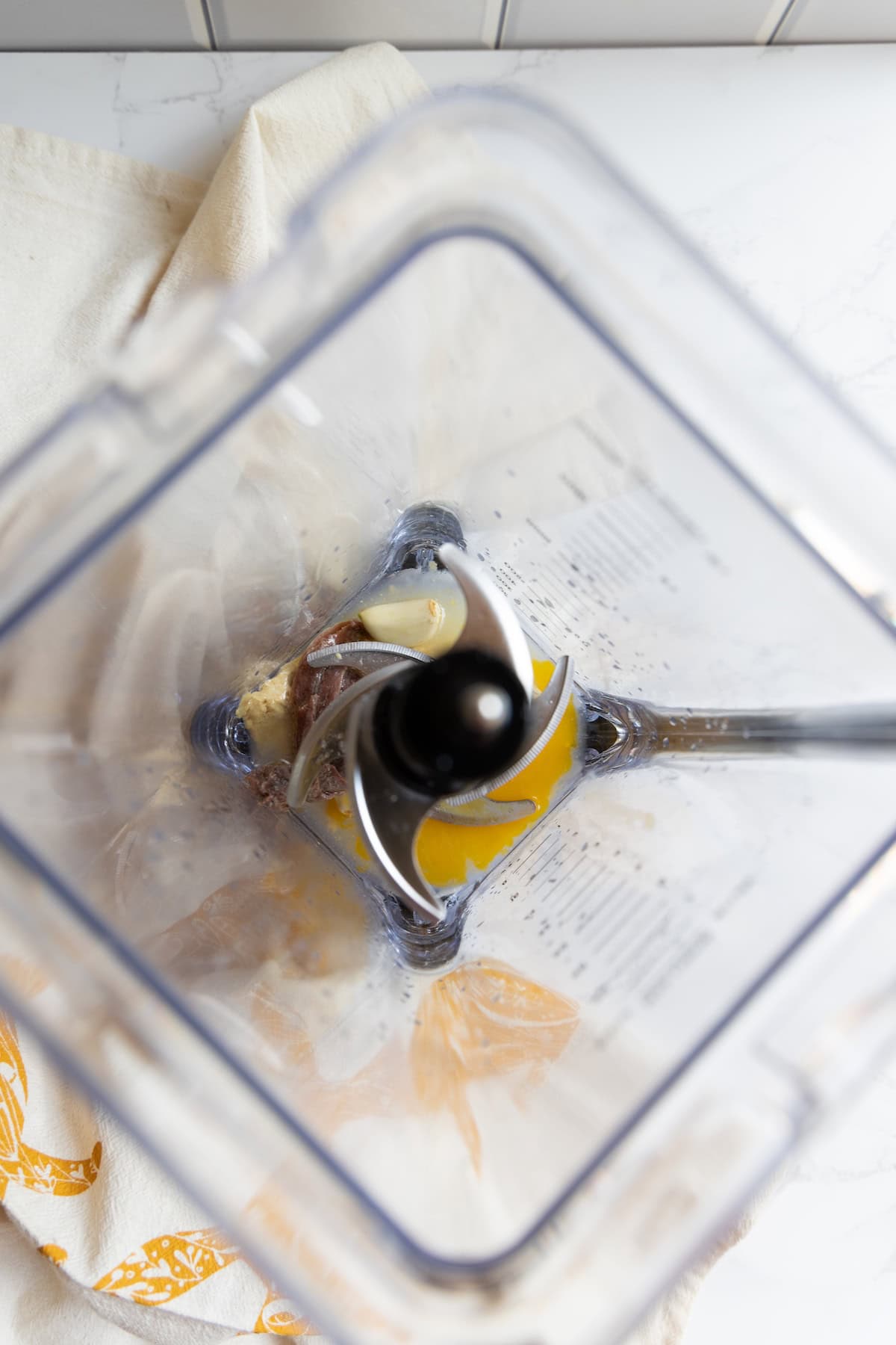 Top view of an empty blender with streaks of caesar dressing residue left on the sides, sitting on a white counter with a beige and orange towel underneath.