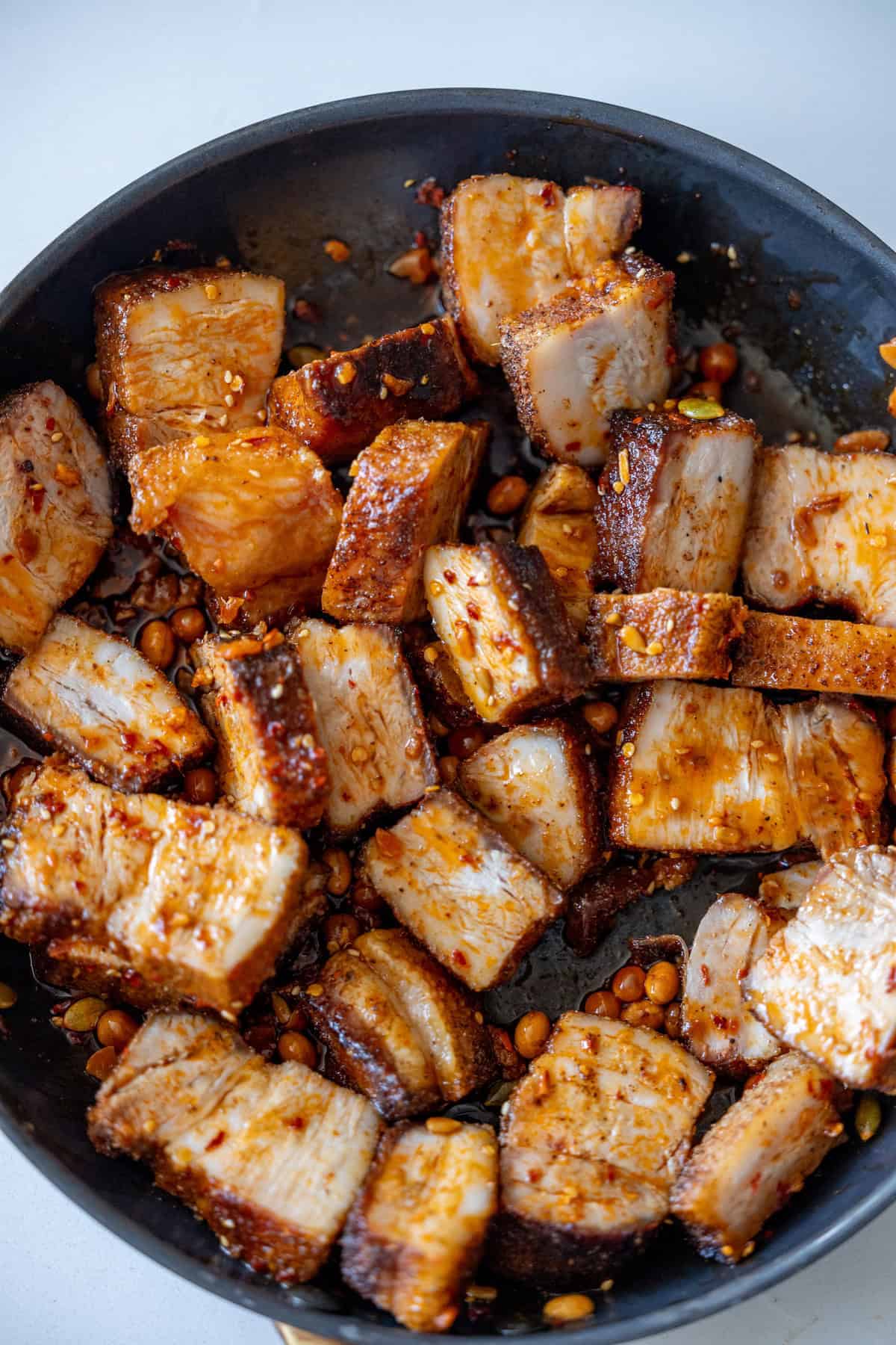 Pan of cooked, cubed Sticky Asian Pork Belly pieces with a spicy seasoning and some peanuts, showing a crispy texture and golden-brown color.