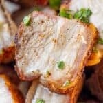 Close-up of crispy, roasted pork belly slices garnished with chopped fresh herbs.