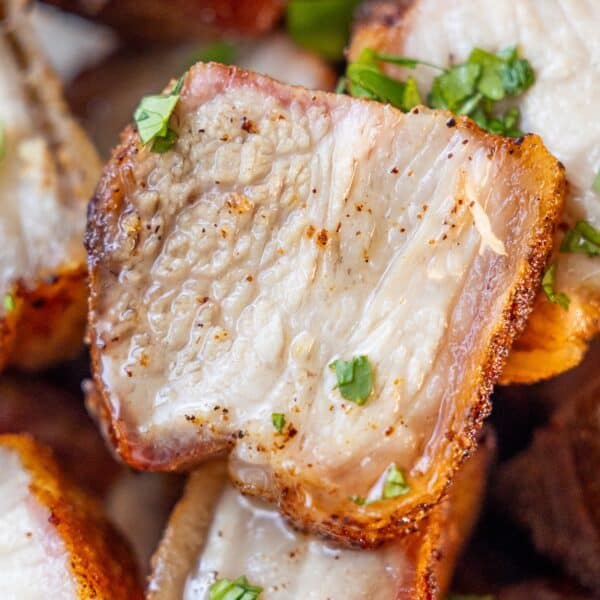 Close-up of crispy, roasted pork belly slices garnished with chopped fresh herbs.