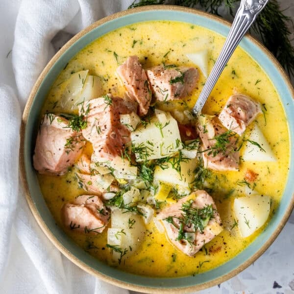 A bowl of creamy Finnish Salmon Chowder (lohikeitto) with chunks of salmon, potatoes, fresh dill, and a spoon, set on a white surface with a napkin.