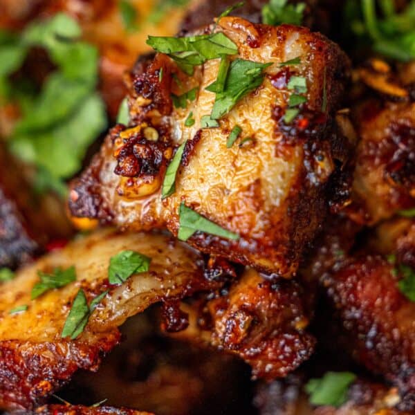 Close-up of seasoned, grilled chicken pieces topped with chopped fresh herbs, served alongside Sticky Asian Pork Belly Bites for a flavorful combination.