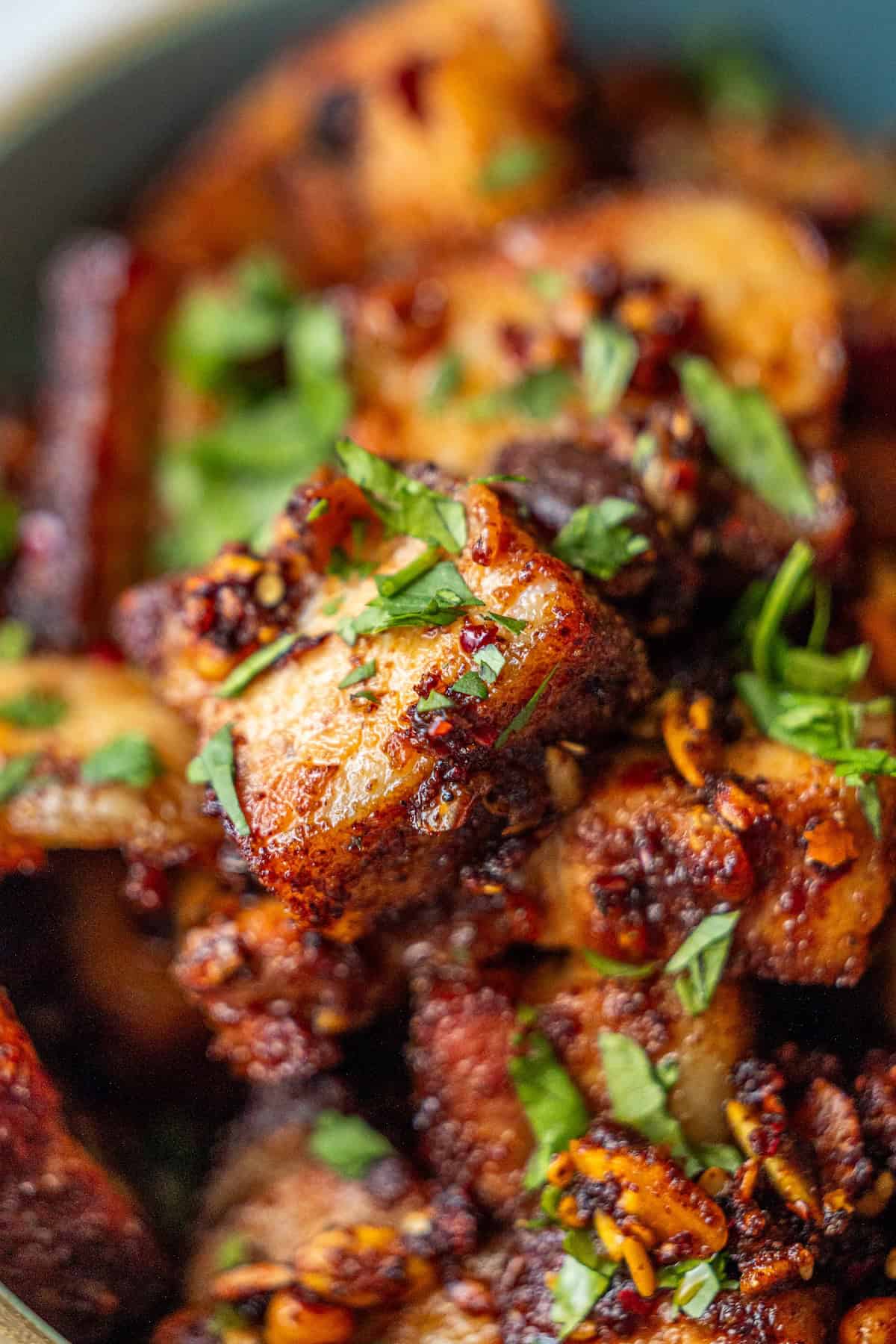 Close-up of crispy, spiced potato cubes garnished with chopped fresh herbs, served alongside tender Sticky Asian Pork Belly.