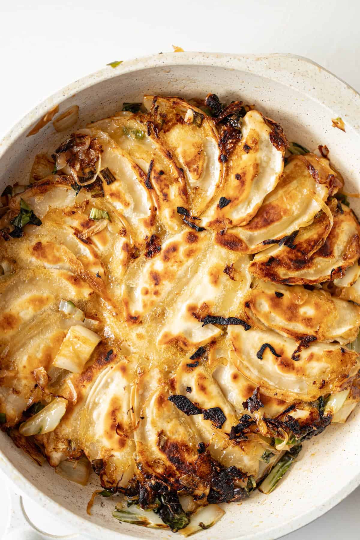 A skillet filled with browned and crispy fried potstickers arranged in a circular pattern.