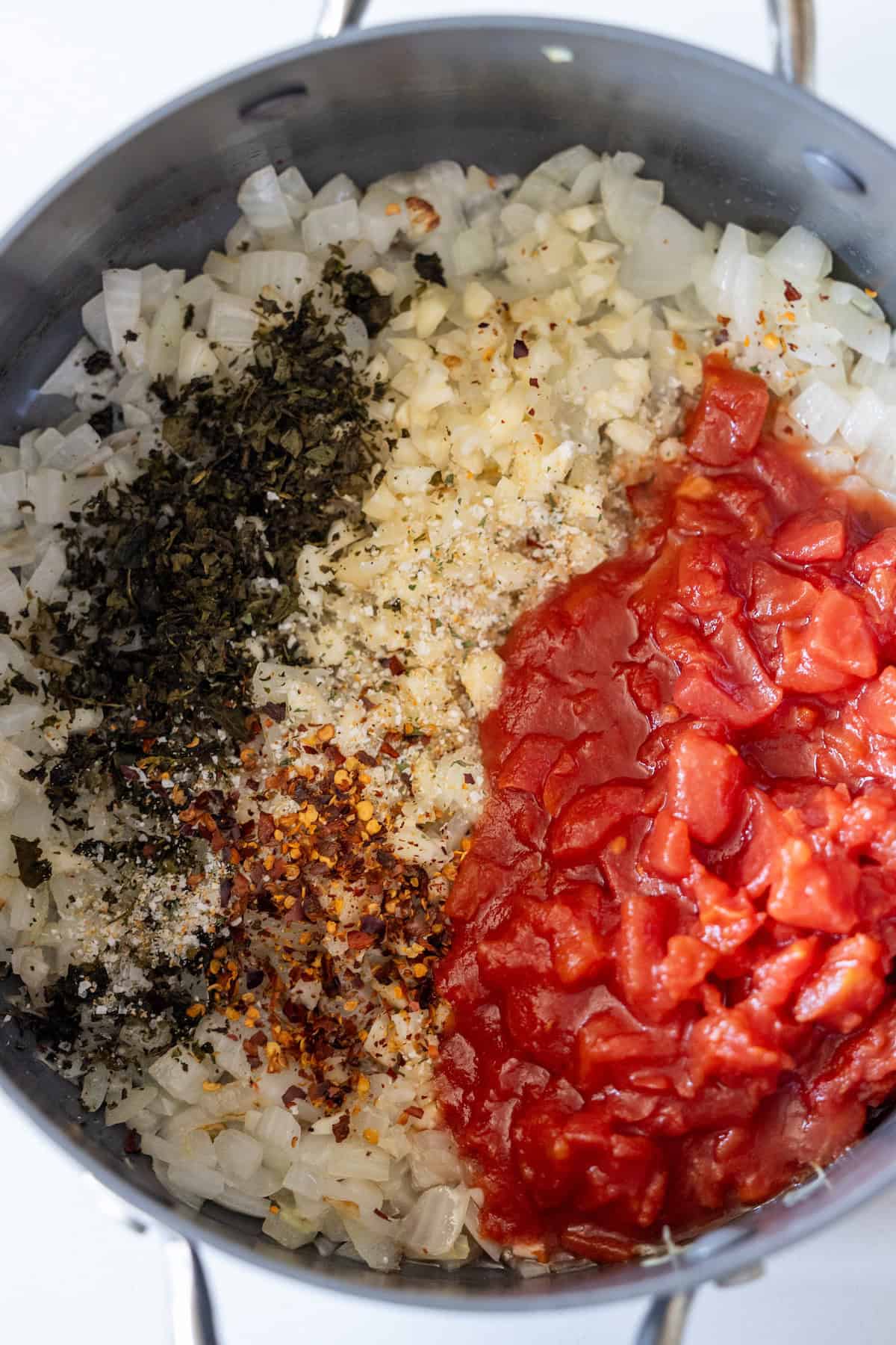 A saucepan containing sautéed diced onions, dried herbs, red pepper flakes, beans, and chopped tomatoes, arranged in separate sections before mixing—a vibrant base perfect for exploring zucchini recipes.