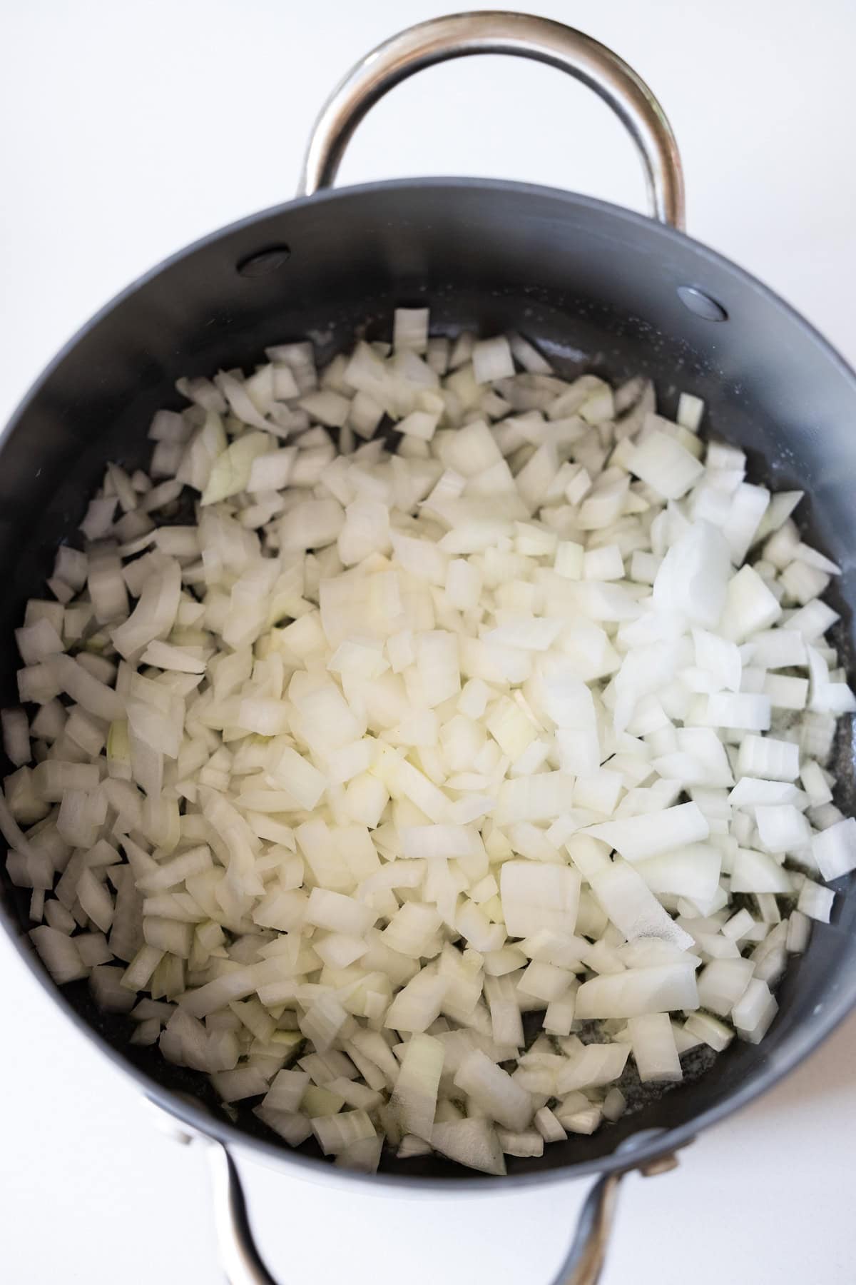 Chopped onions and zucchini in a large black pot with metal handles, ready for cooking.