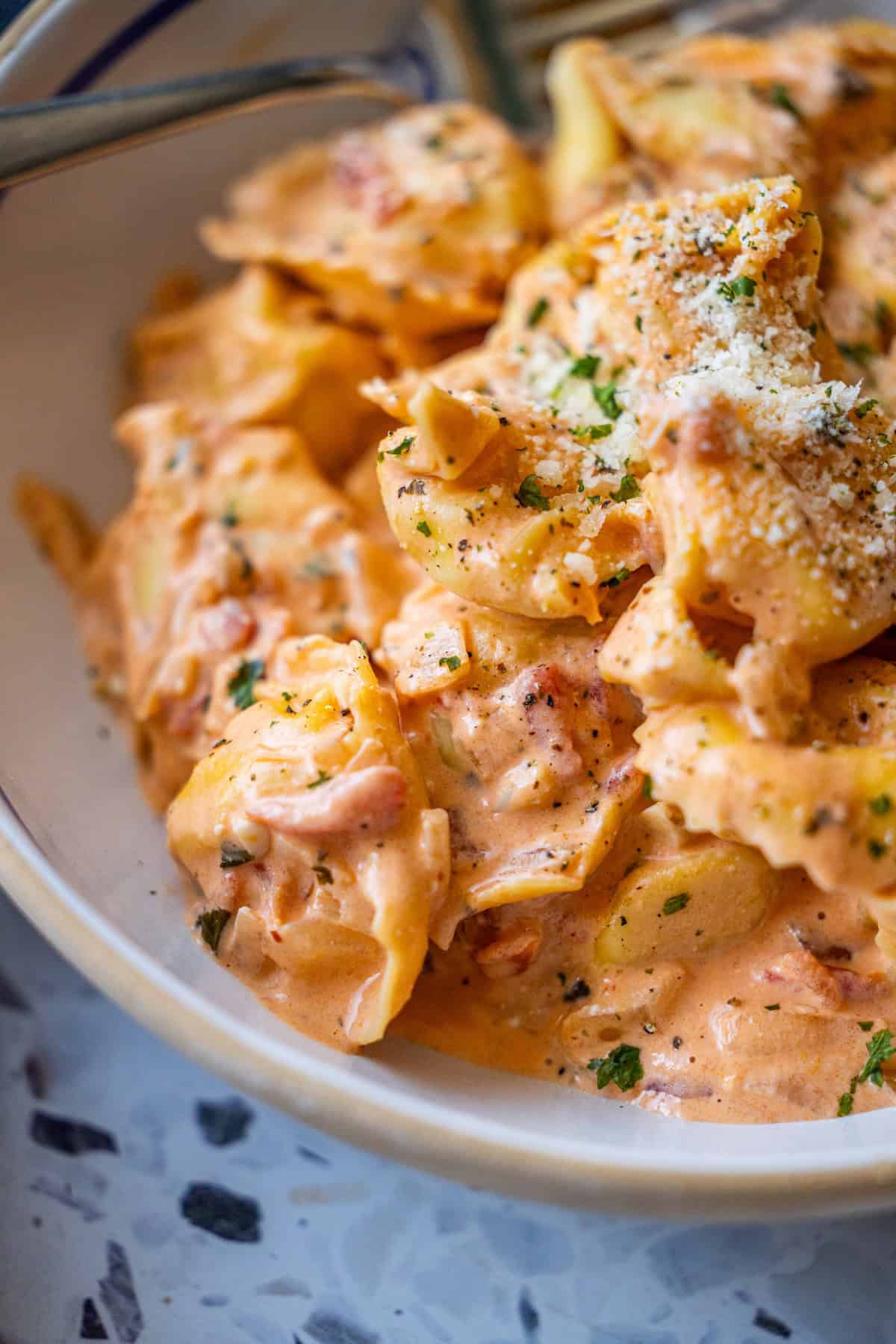 A close-up of creamy tortellini in a rich tomato sauce, garnished with grated cheese and chopped herbs, served in a bowl—perfect for trying a Marry Me Tortellini recipe.