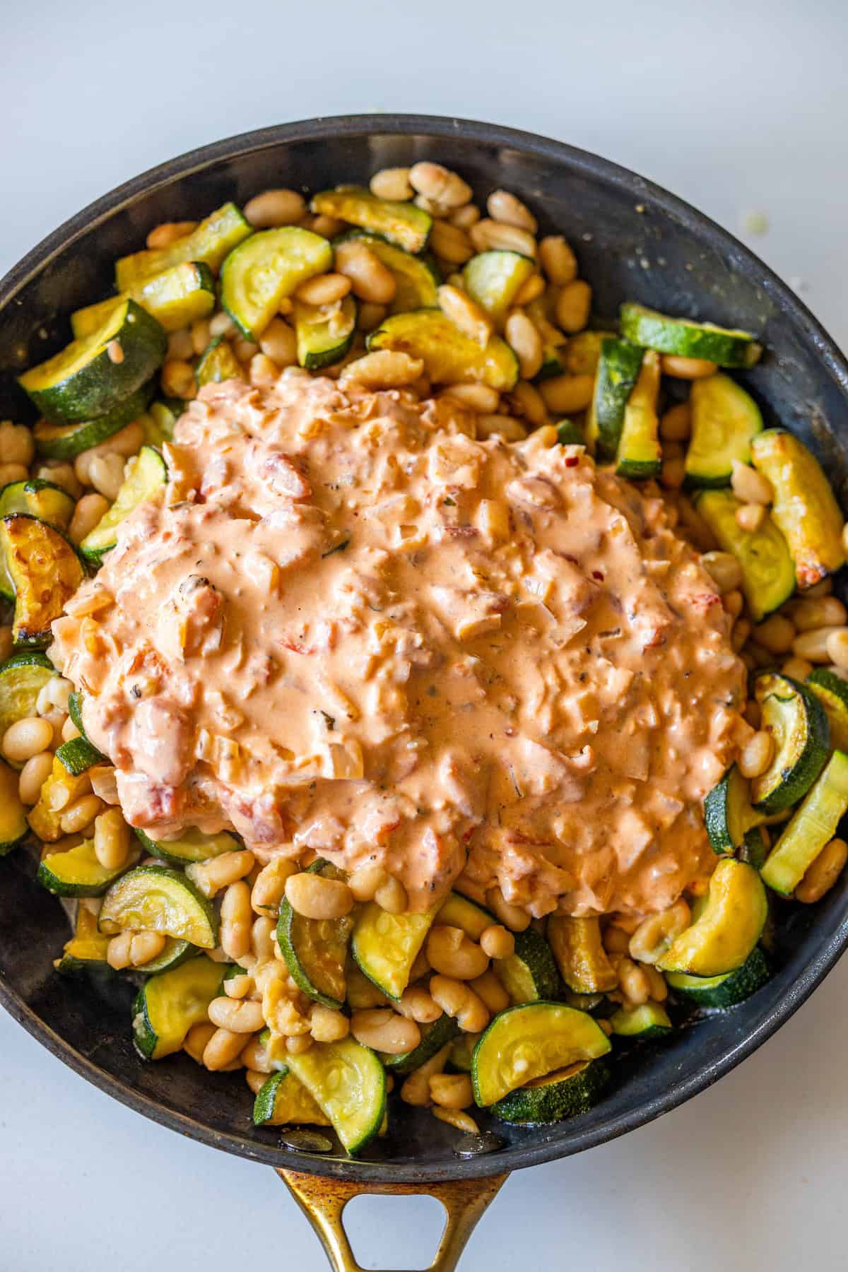Skillet with sautéed zucchini and beans, topped with a creamy Marry Me tomato-based sauce.