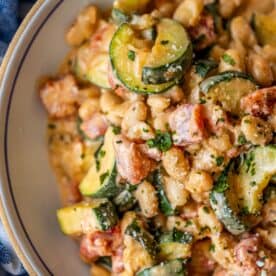 Close-up of a bowl containing a creamy mixture of beans, zucchini slices, diced tomatoes, and herbs—flavors that truly marry me in every bite.