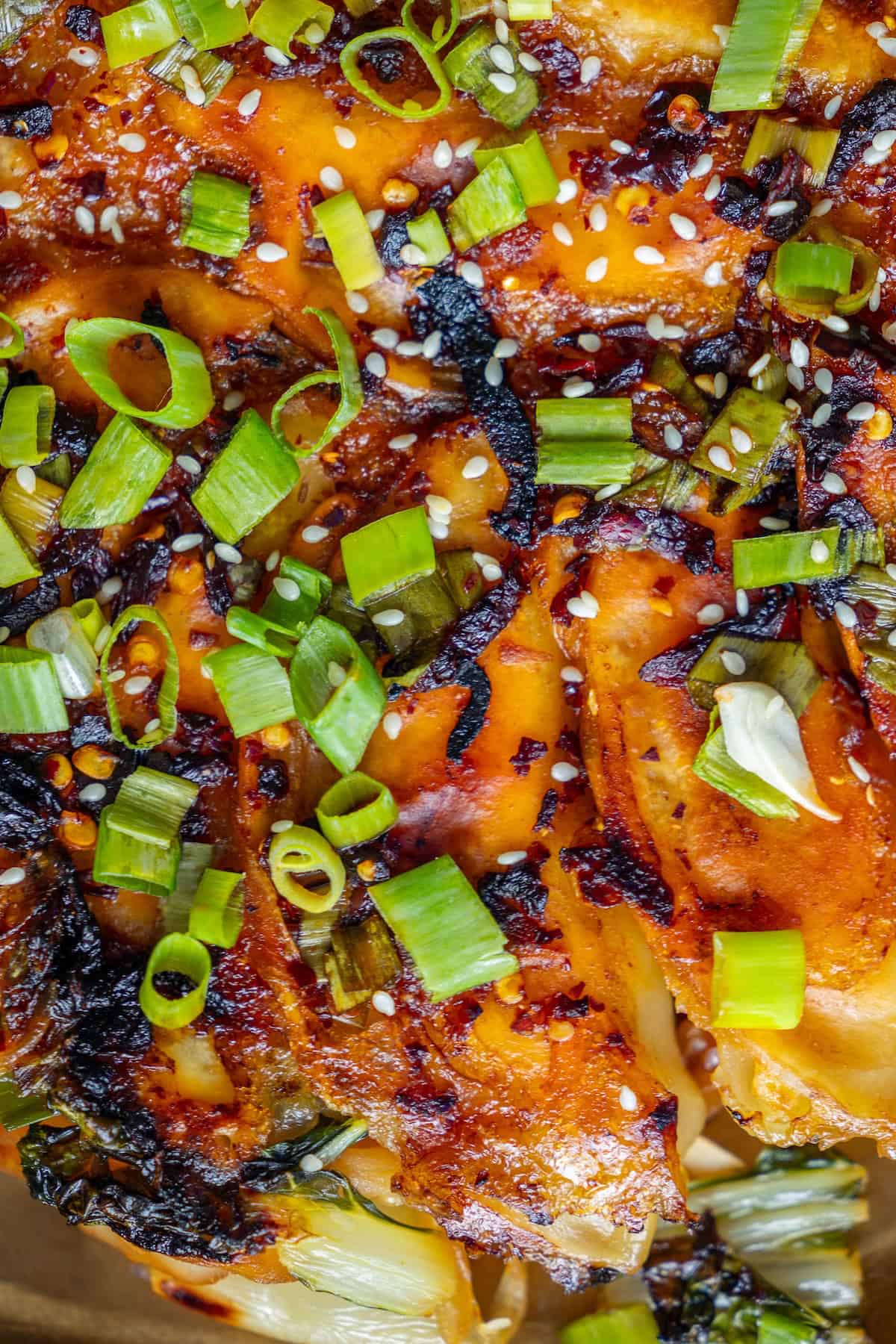Close-up of grilled chicken topped with chopped green onions, sesame seeds, and a caramelized glaze, served alongside a crispy Bok Choy Pancake.