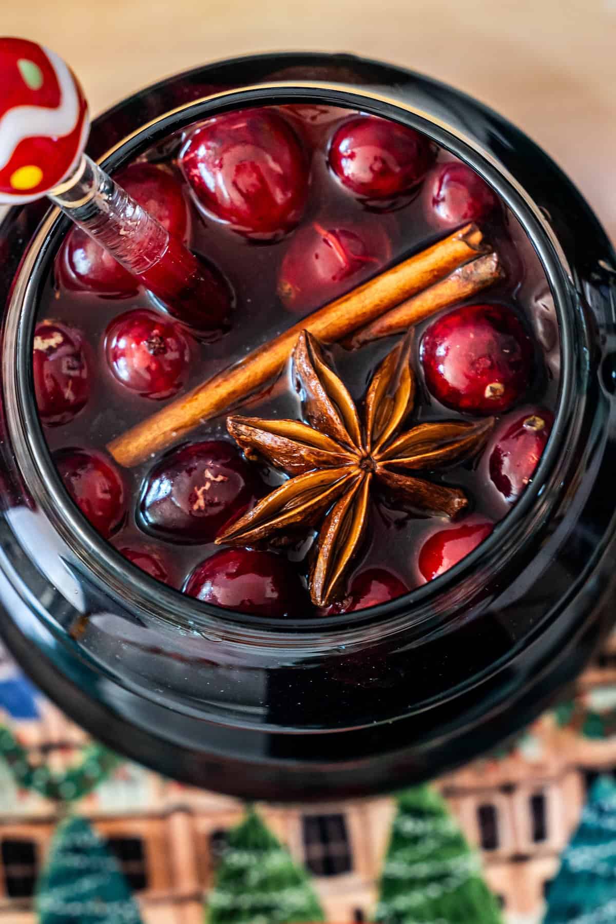 Close-up of a glass jar filled with Mulled Cranberry Cider, garnished with cranberries, a cinnamon stick, star anise, and a decorative straw.