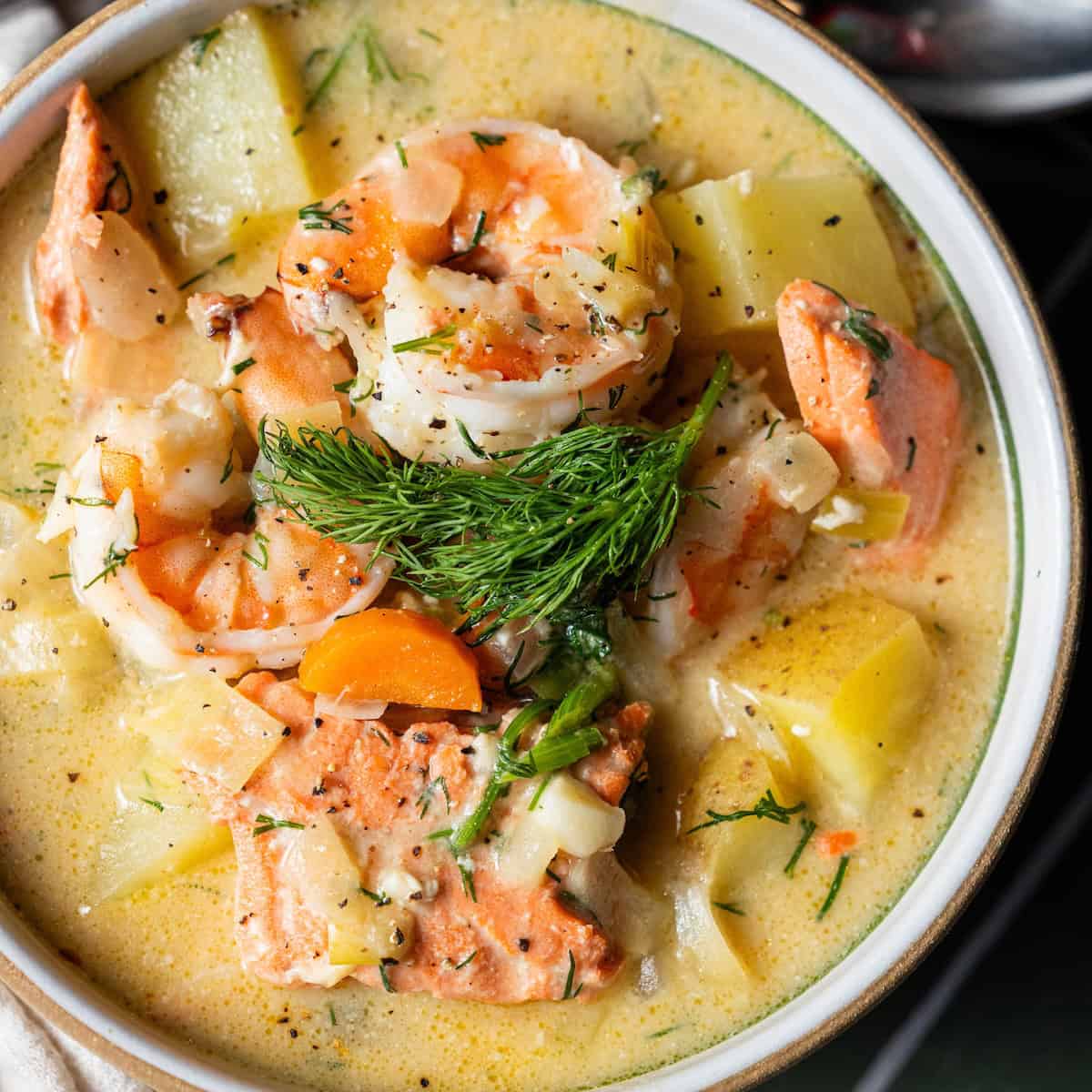 A bowl of creamy Irish Seafood Chowder with shrimp, salmon, potatoes, carrots, herbs, and a sprig of fresh dill on top.