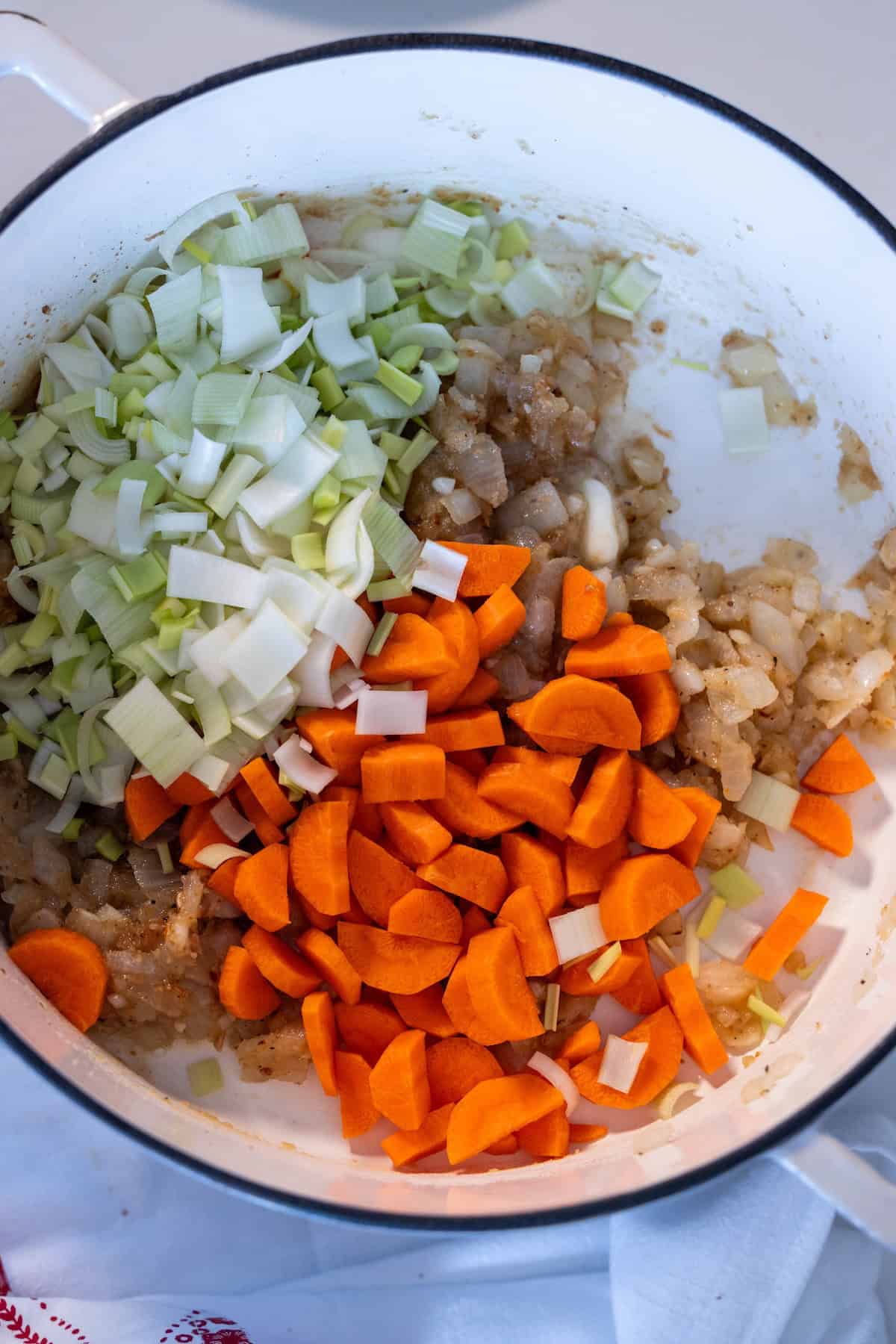 Chopped onions, carrots, and leeks are in a white pot, partially cooked and ready to become the savory base for a classic Irish Seafood Chowder.