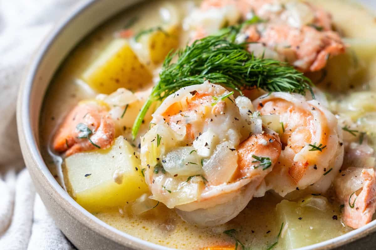 A close-up of a bowl of Irish Seafood Chowder featuring shrimp, salmon, diced potatoes, onions, and fresh dill in a creamy broth.