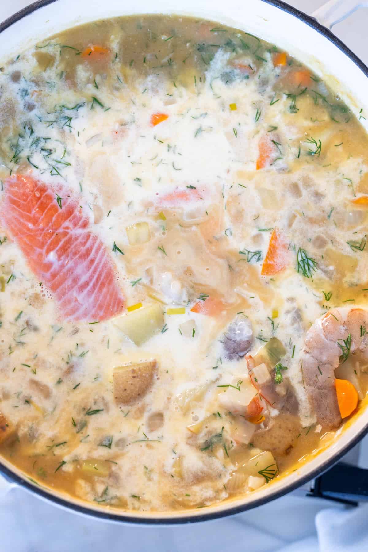 A pot of creamy Irish Seafood Chowder with chunks of salmon, potatoes, carrots, fresh dill, and other vegetables simmering together.