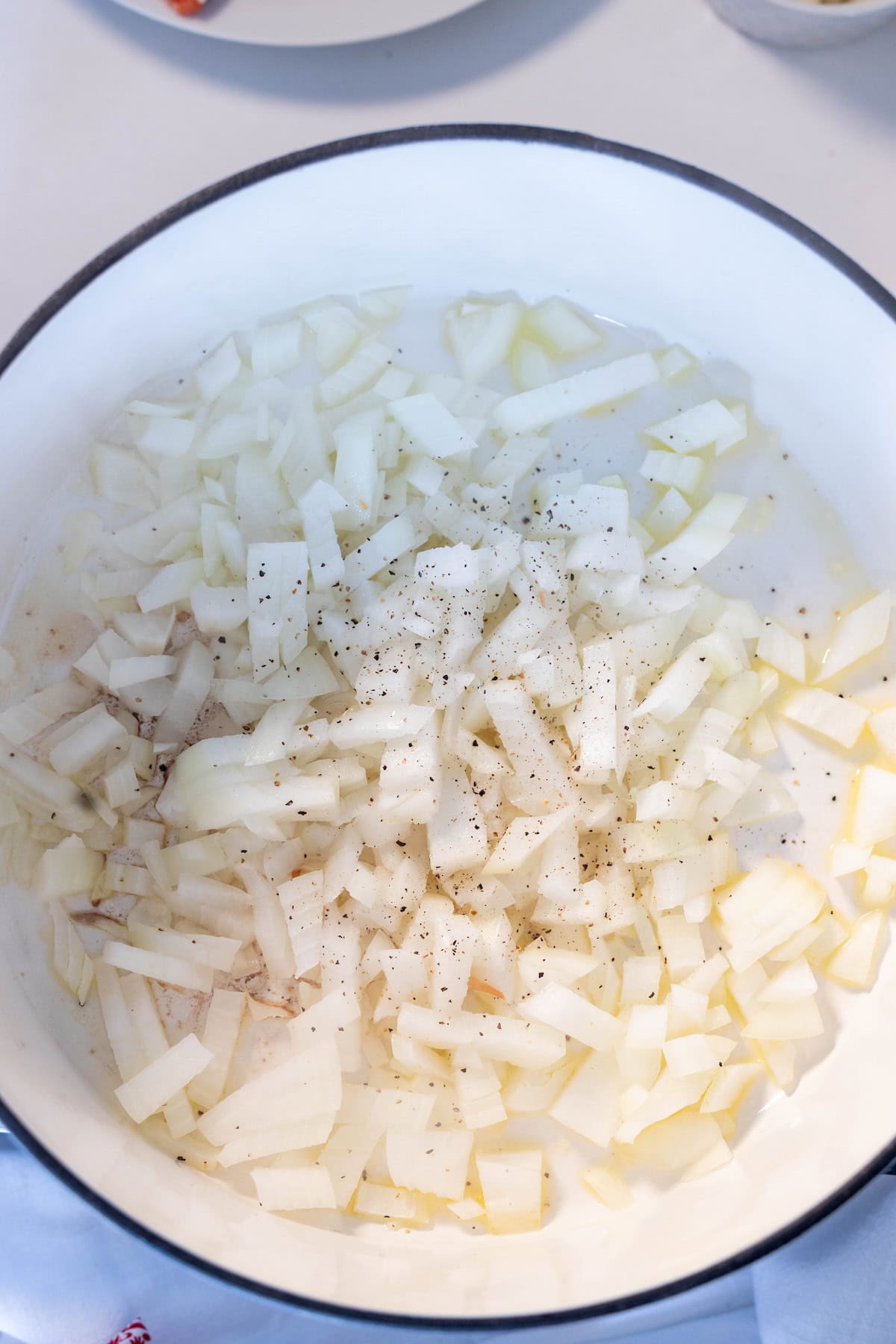 Chopped onions and ground black pepper sizzle in a white pot with oil, forming the perfect base for a hearty Irish Seafood Chowder.
