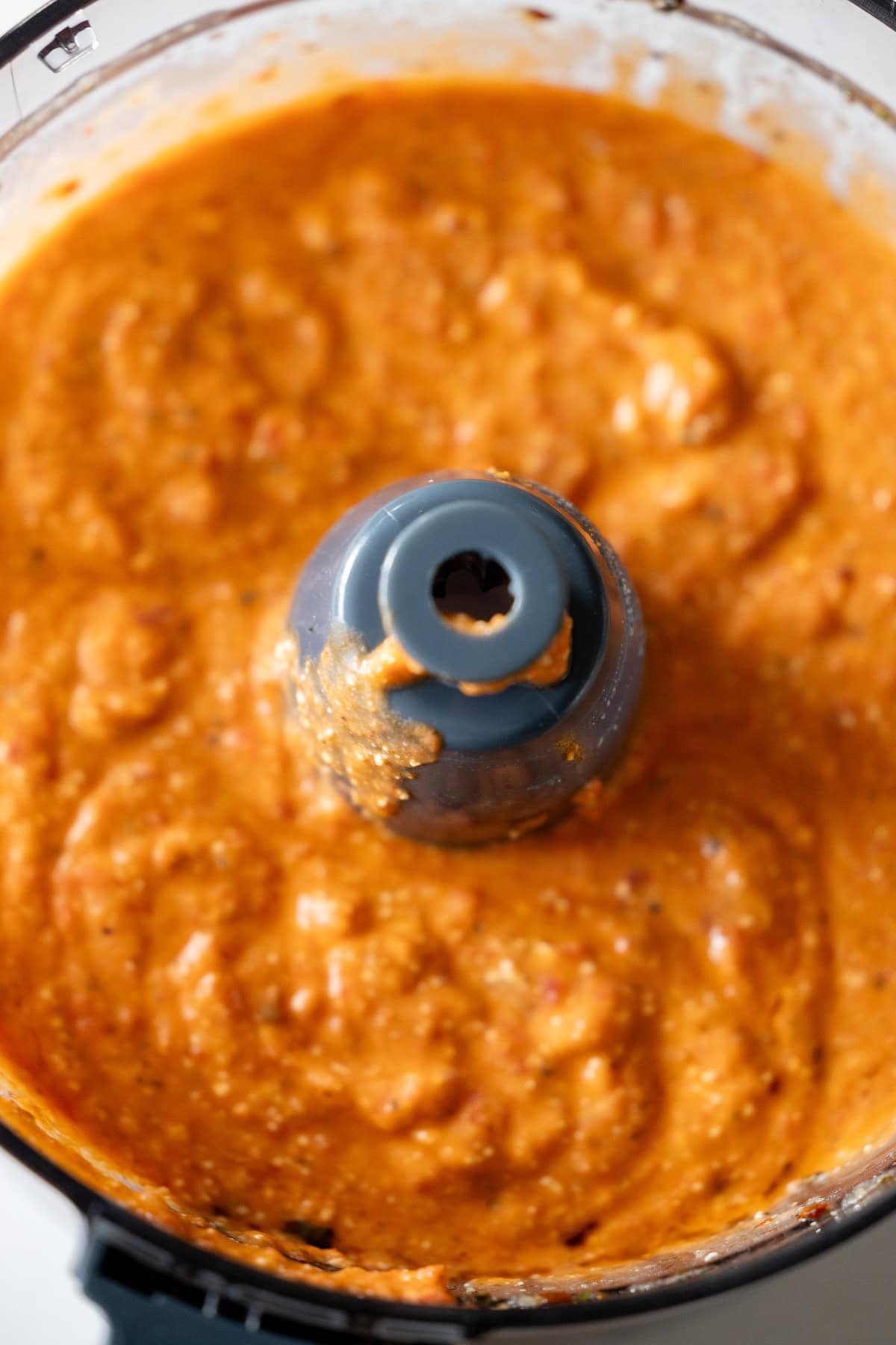 An overhead view of thick, orange-red sauce blended in a food processor.