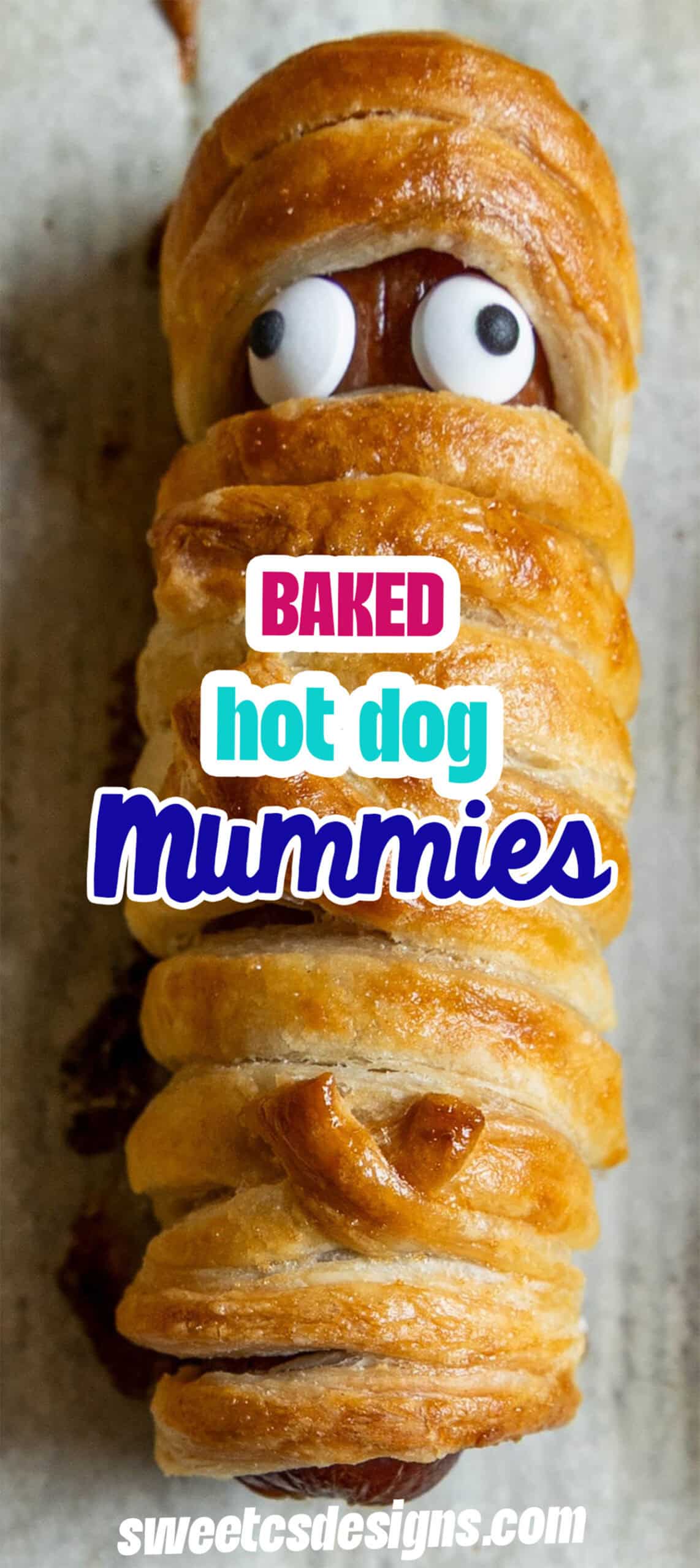 A mummy hot dog wrapped in golden baked pastry with candy eyes peeks out. Text over the image reads: “Baked hot dog mummies.”.