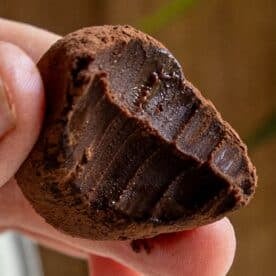 A hand holding a bitten chocolate truffle coated in cocoa powder, revealing the smooth, rich, dark chocolate filling inside—perfect for chocolate truffles lovers.